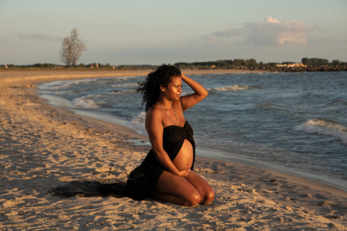 portfolio zwangerschap vrouw zittend op het strand met kunstwerk achtergrond